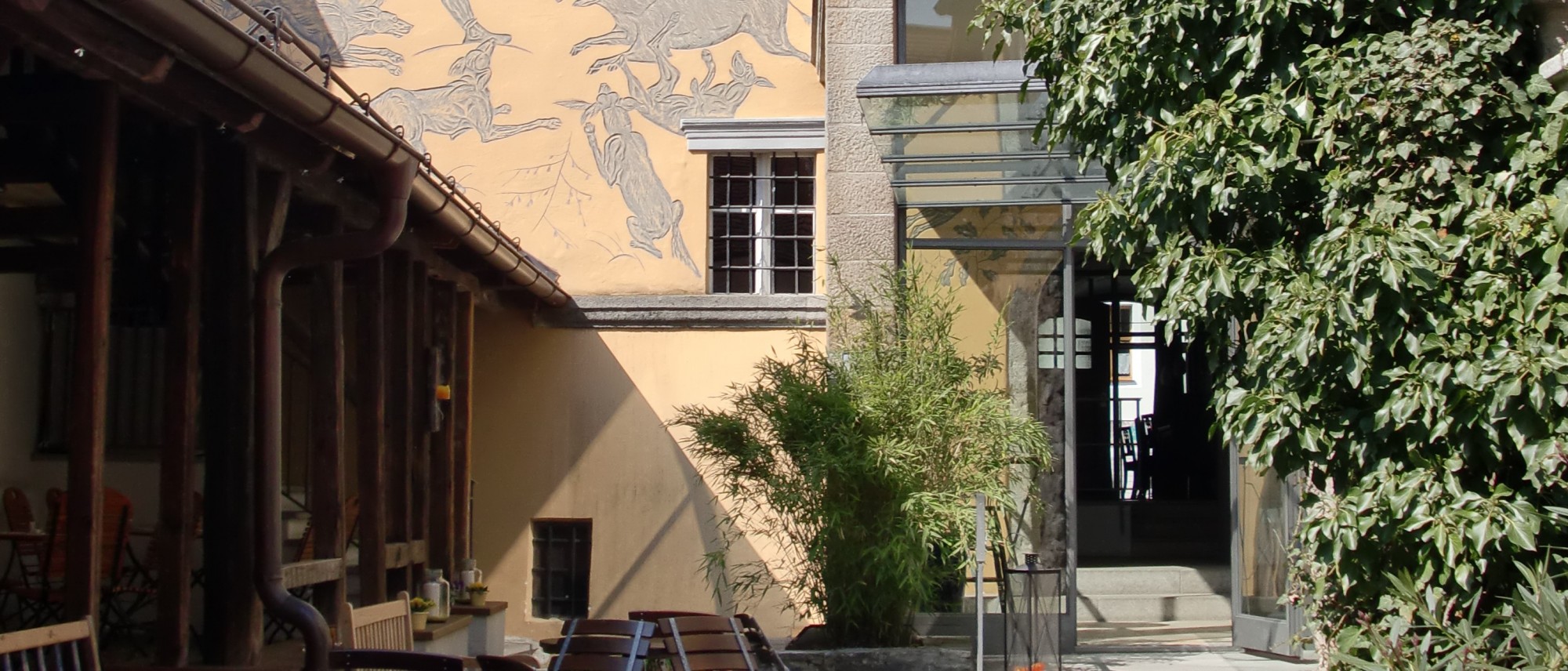 Das Foto zeigt im Ausschnitt den rückwärtigen Innenhof des Schmidt-Haus. Blick auf die Ostfassade, eine Säulenveranda und links die ehemalige Holzlege, jetzt Außenbereich des Cafés.