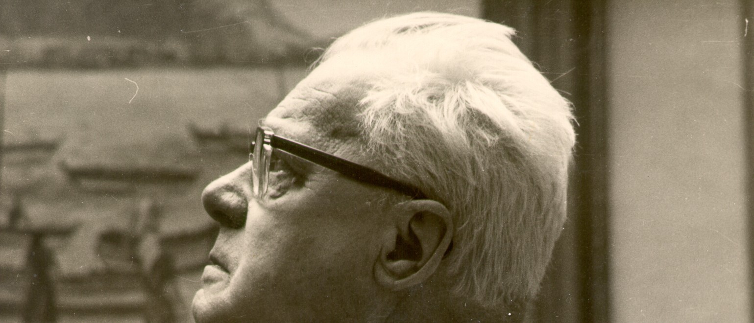 Das schwarz-weiß-Foto zeigt den Kopf von Karl Schmidt im Profil und mit Hornbrille. Im Hintergrund verschwommen eines seiner Bilder.