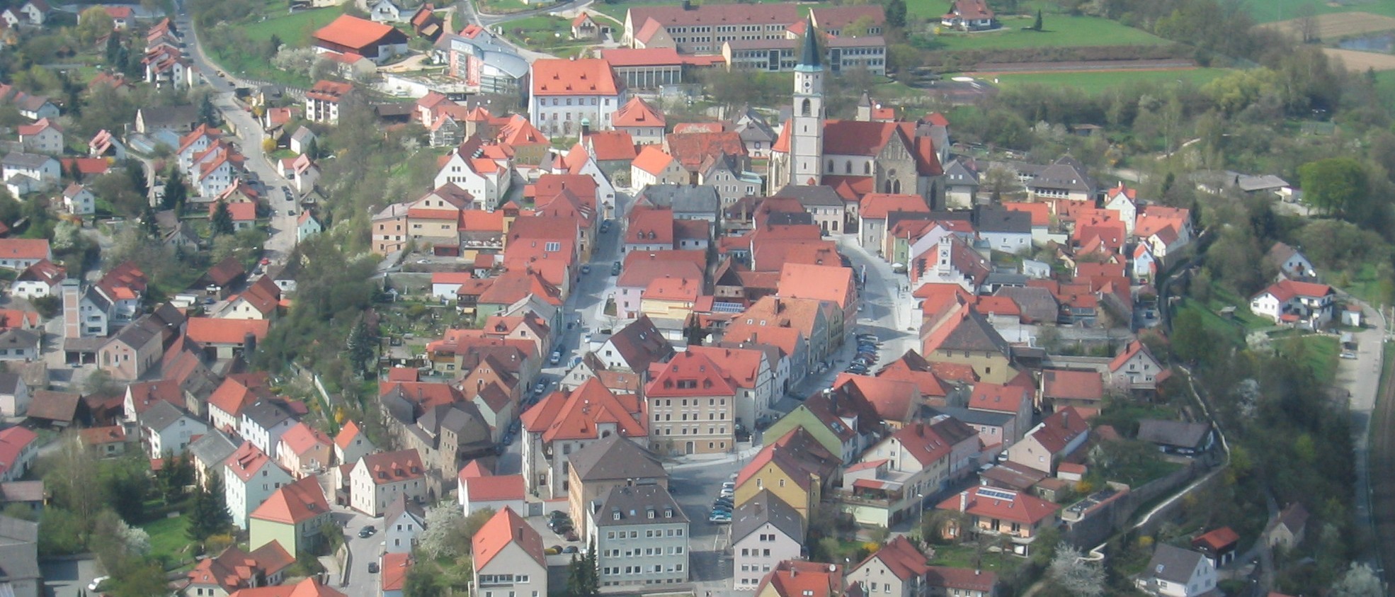 Das Foto zeigt die Altstadt von Nabburg aus der Vogelperspektive. Am oberen Bildrand in der Mitte erhebt sich die Stadtpfarrkirche auf dem höheren Areal des Hochplateaus.
